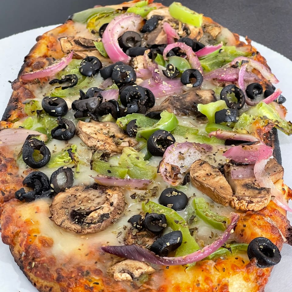 Cheesy vegetable pizza topped with mushrooms, black olives, green peppers, and red onions on a white plate.