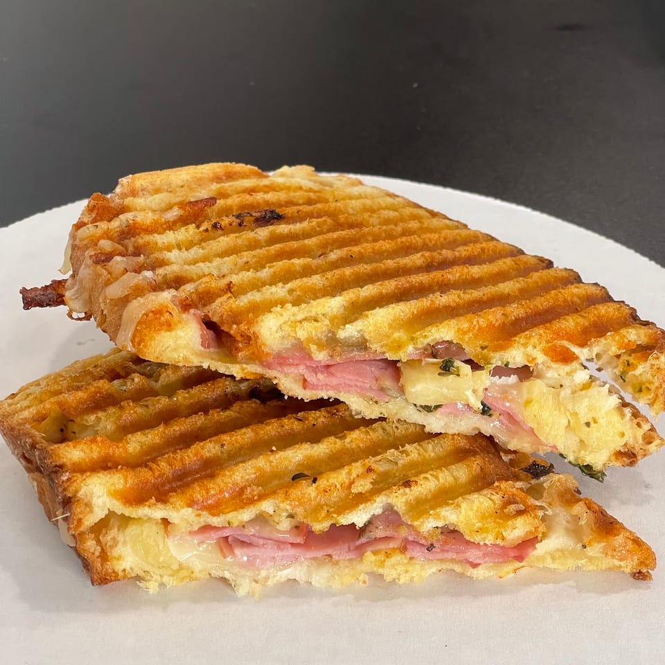 Grilled panini halves reveal layers of ham, melted cheese, and pineapple on a white plate.