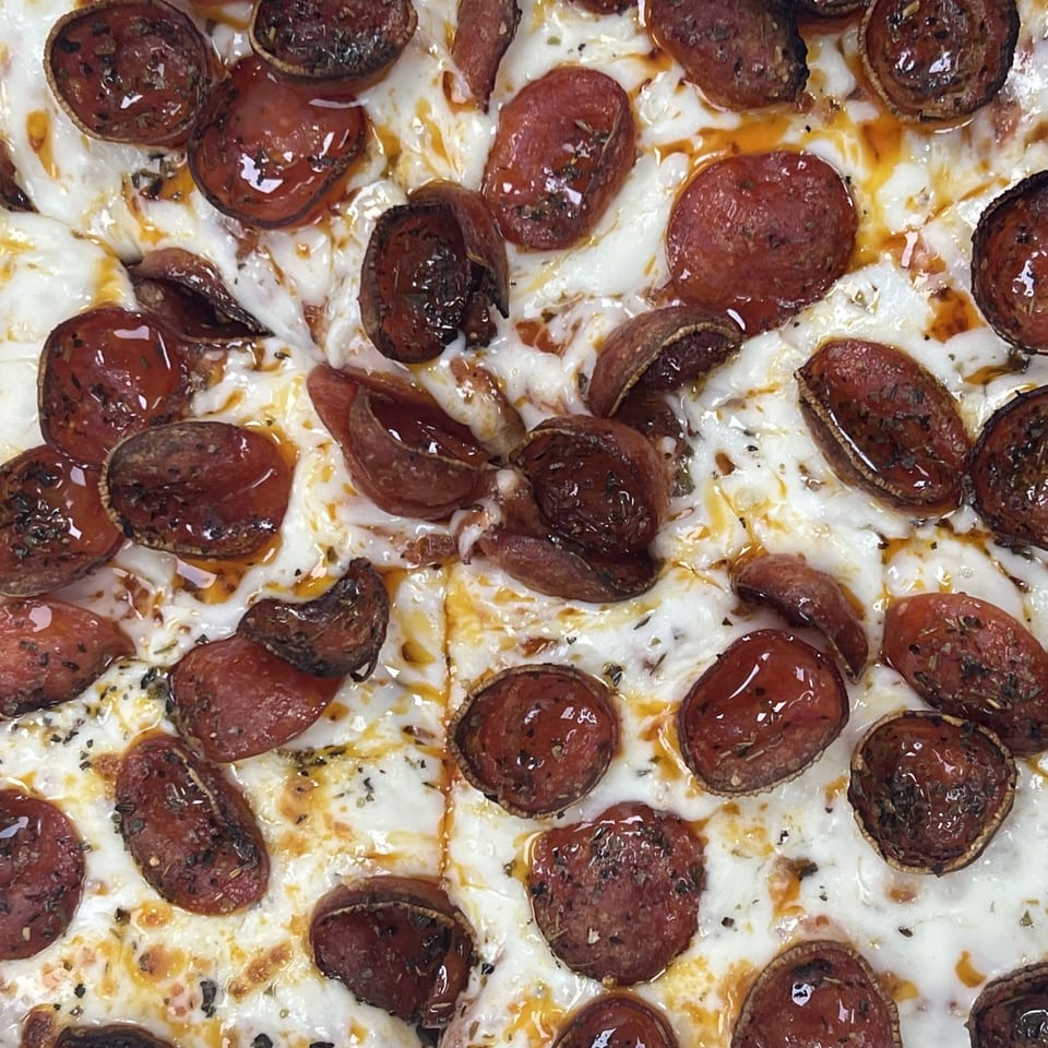 Close-up of a cheesy pepperoni pizza topped with browned pepperoni slices, herbs, and glistening oil.